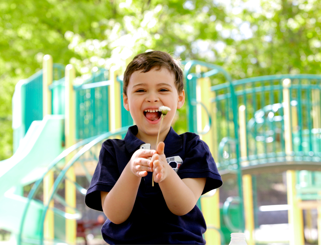 A young boy laughing and holding a flower while playing at a colorful outdoor playground.