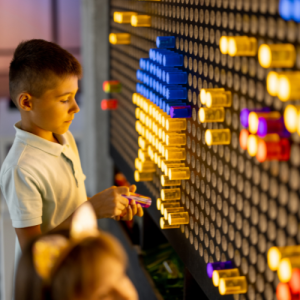 A boy plays with colorful illuminated pegs on a light board wall.
