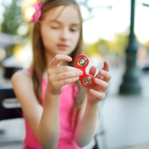 A young girl holds a red fidget spinner, focusing intently.