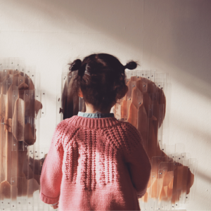 A toddler in a pink sweater explores a textured wall installation.
